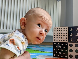A 3-month-old baby lying on their tummy, attentively gazing at black-and-white contrast cards. The baby’s curious expression and focused gaze highlight early cognitive and visual development.
