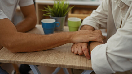 Men having a heartfelt conversation in a cafe with hands touching across the table, signifying...