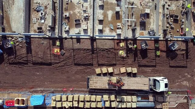 Aerial view from drone at construction site showing delivery truck offloading bricks and blocks materials for building development