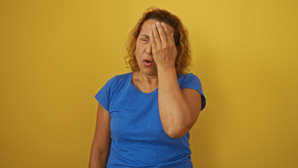 Elderly hispanic woman with curly hair in a blue shirt isolated against a yellow background,...