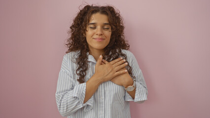 Young woman with hands on heart over isolated pink background, displaying gratitude and happiness