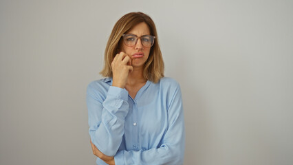 Attractive young woman in glasses and blue shirt over isolated white background, looking thoughtful and concerned while holding her chin.