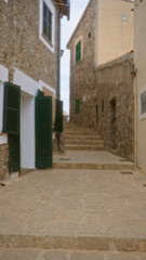 Blurred outdoor scene in mallorca, spain, featuring a defocused view of rustic stone buildings with green shutters and stone steps in a narrow alleyway