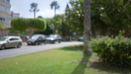 Obraz premium Blurred background in an outdoor city setting with cars, greenery, trees, and buildings in soft focus.
