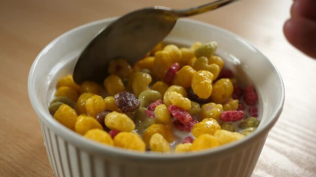 slow motion scooping colorful fruity cereal with a spoon from a bowl full of milk