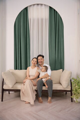 Obraz premium Young parents are playing with their 10 -month -old son on the sofa, Green curtain at the back