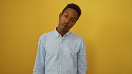 Young african man posing playfully against a yellow background, showcasing his attractive features in a casual setting.