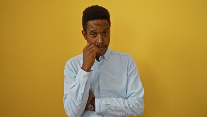 Young man posing contemplatively over isolated yellow background wearing blue shirt conveying thoughtful and attractive demeanor suggesting introspection and confidence.