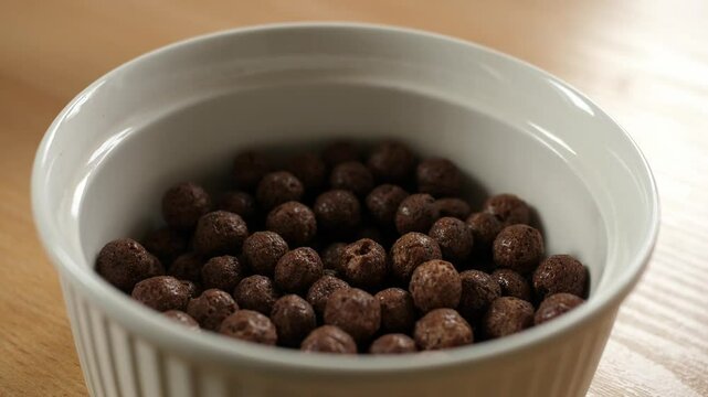 pouring brown chocolate choco cereal balls into an empty white bowl