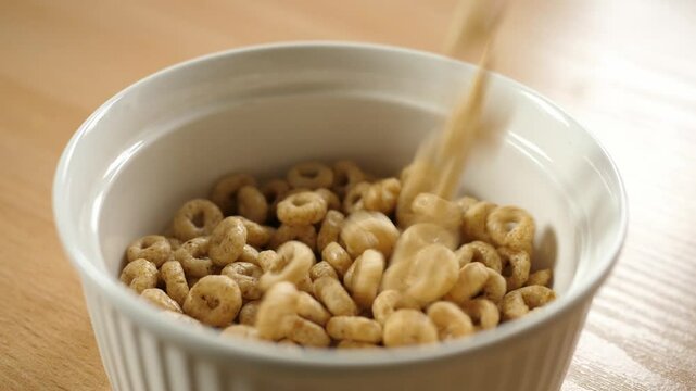 slow motion pouring honey cereal circles rings into an empty white bowl