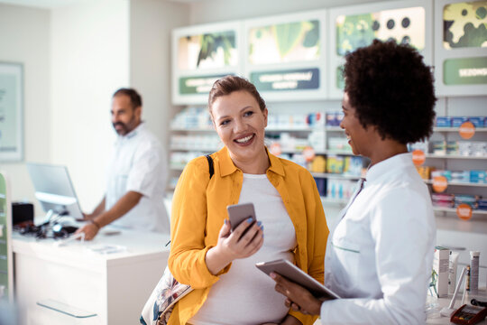 Female pharmacist helping pregnant woman in drug store