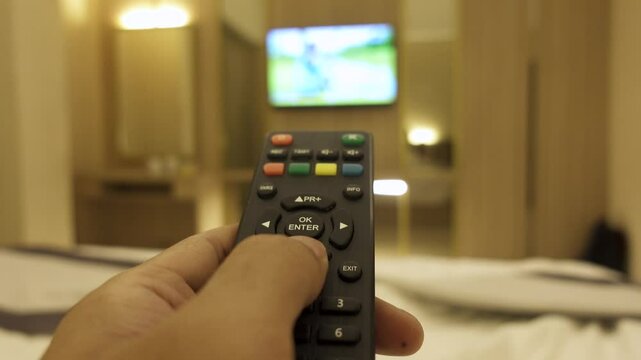 A man's hand changes television channels in a room. Changing channels with remote