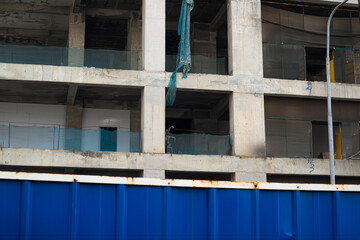 An unfinished concrete building stands tall against a cloudy sky. The exposed structure and surrounding debris depict an incomplete construction project.