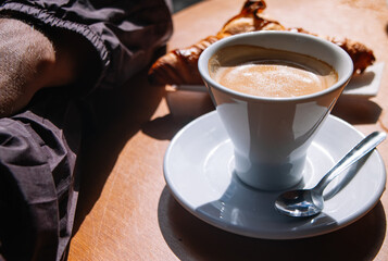 Hands of a man next to a delicious coffee and a tasty croissant in the background on a French-style breakfast morning.