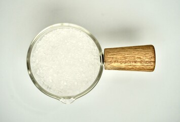 Pile of salt food flavoring ingredient in glassware cup with wooden handle isolated on horizontal white background from above top angle view.