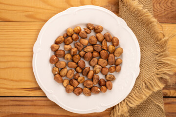 Hazelnuts in a white plate on a wooden table, close-up, top view.