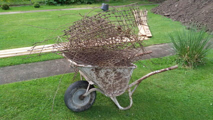 Alte Schubkarre mit Baustahl-Schrott beladen, im Garten auf einer Wiese.