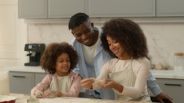 Happy African American family at home kitchen woman man and little girl father cuddling hugging child kid daughter mother show dough flour cooking cookies cook baking pastry together talking insurance