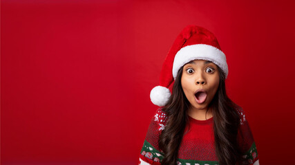 Fototapeta premium Surprise discount: girl Santa Claus with open mouth on a red background. A surprised man in a Christmas costume makes a funny face, isolated on a banner with copy space