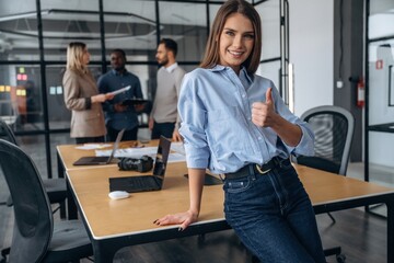 Cheerful woman is standing. Professional workers are in the modern office together