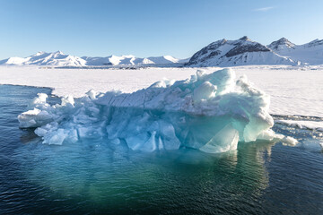 Blue glacial iceberg at the edge of the fast ice, Nordfjorden fjord. Svalbard. Much of the submerged iceberg can be seen in the crystal clear waters.