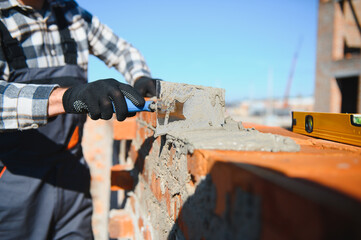 construction mason worker bricklayer installing red brick with trowel putty knife outdoors