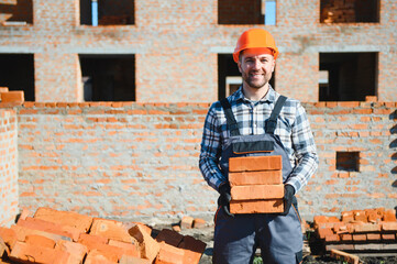 Young adult man builder working at object carrying bricks at construction site