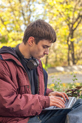 A student studies using a laptop. Male student studying online outdoors.