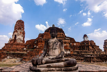 A statue of Buddha is sitting on a stone platform in front of a large building