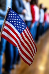 A close-up of a US flag in the foreground, with people lined up in the background, emphasizing patriotism and community engagement.