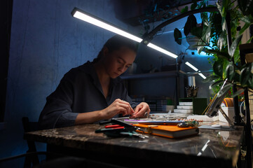 Top view artistic female hands creating bracelet from stones. POV shot of woman working with craft. Accessories on workshop table close up