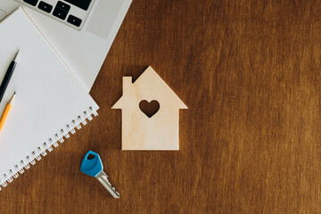 Wooden house, key and laptop on the wooden table, top view, tax concept.