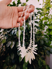 Mother of pearl necklaces in hand, holding irregular stone chokers, floral background, nacre...