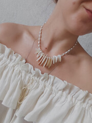 Woman in white open shoulder blouse, mother of pearl necklace, irregular stone choker on women's...