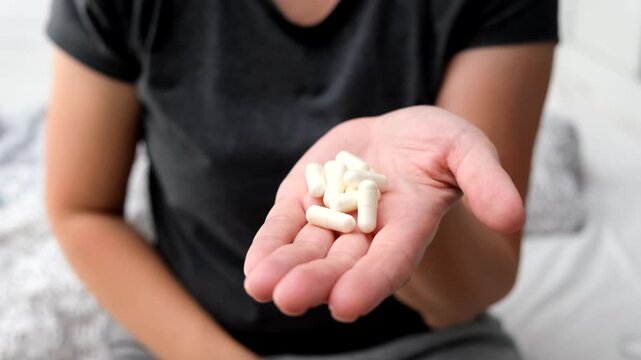 White capsules or Tablets in the hand and on the palm of a girl or woman, close-up. Taking vitamins, painkillers, medications, and dietary supplements.