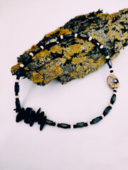 Black stone beaded necklace at pink background close up on tree bark with lichen arrangement....