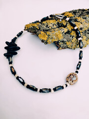 Black stone beaded necklace at pink background close up on tree bark with lichen arrangement....