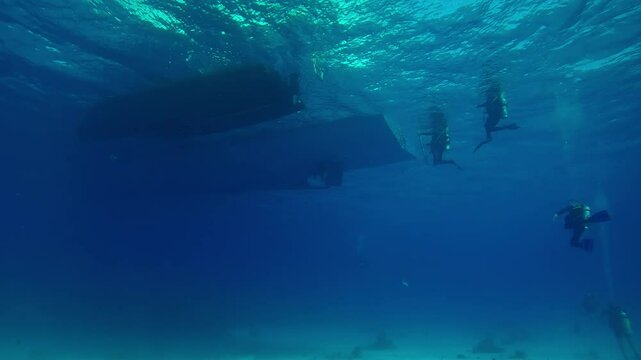 Group of scuba divers approaching the ramp and boarding a diving boat on a sunny day, Slow motion of divers returning underwater to their diving safari boats, Underwater view
