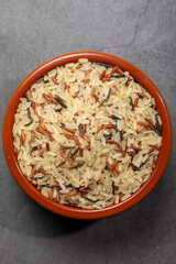 Earthenware bowl full of long, red, wild rice on a kitchen countertop in a zenithal photograph