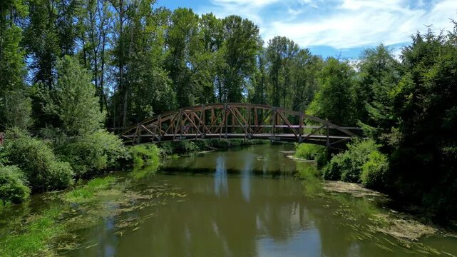 Aerial view drone flying at footbridge in Bothell Washington. People walking across footbridge over river in small town. 