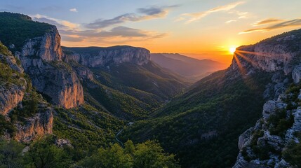 Naklejka premium Majestic sunset over a mountain valley, with dramatic cliffs and lush greenery.