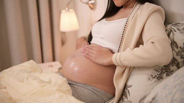 Beautiful pregnant woman applying cream on belly