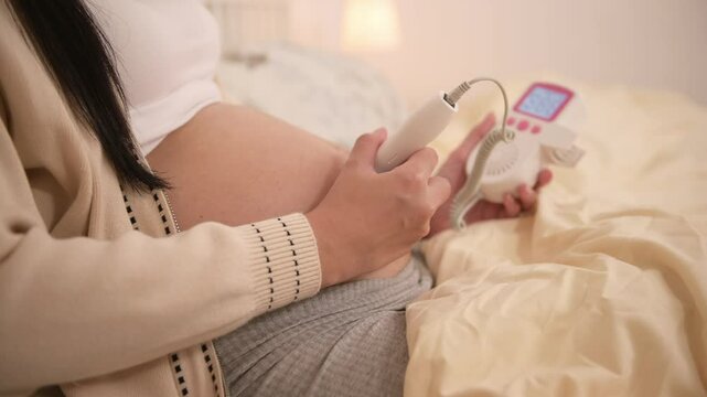 Pregnant woman holding pocket fetal doppler to listen baby heartbeat on belly