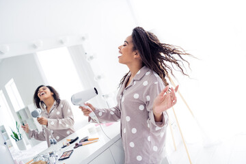 Naklejka premium Young woman with afro hair enjoying morning routine in pajamas with hairdryer