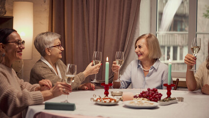 Happy birthday. Elderly woman meeting at home to celebrate birthday of friend, raising glasses of wine in celebratory toast. Concept of elderly lifestyle, positive emotions, holiday