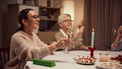Smiling elderly women sitting table decorated with candles and plate with snacks, appetizers, drinking wine, saying toast and celebrating. Concept of elderly lifestyle, positive emotions