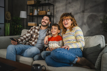 Mum, dad and son watch cartoon or movie on television and sit on sofa