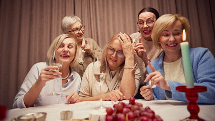 Group of elderly woman, cheerful friends meeting at home, creating cozy moment of friendship and memories, talking and drinking wine. Concept of elderly lifestyle, positive emotions