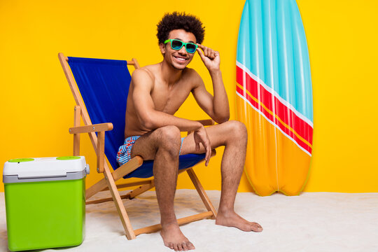 Young man enjoying a relaxing summer day in casual swimwear on a beach chair with vibrant yellow background - Powered by Adobe