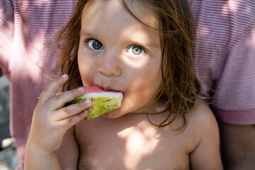 Portrait of a cute baby. The kid eats a watermelon and looks at the camera . Lifestyle. Candid. The concept of an active family holiday. Selective focus. Front view. Close-up. 